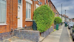 A row of terraced houses with brick facades, satellite dishes, and a well-maintained hedge.