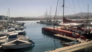 A marina with various boats docked, a clear sky, and a distant mountain range.