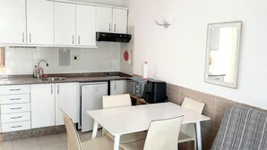 A compact kitchen with white cabinets, a sink, a coffee maker, and a dining table with chairs.