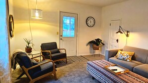 Un salon comprenant un canapé, des fauteuils, une table basse, une plante en pot et une horloge murale.