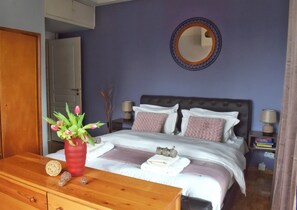 A bedroom with a bed, bedside lamps, a mirror, a wooden dresser, and a vase with flowers. - 4-bedroom Athens Smart Stay - Base Rate - Extra Customisable (Athens)