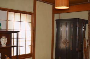 A traditional Japanese room with tatami flooring, a shoji screen, a dark wooden cabinet, and a hanging lamp.