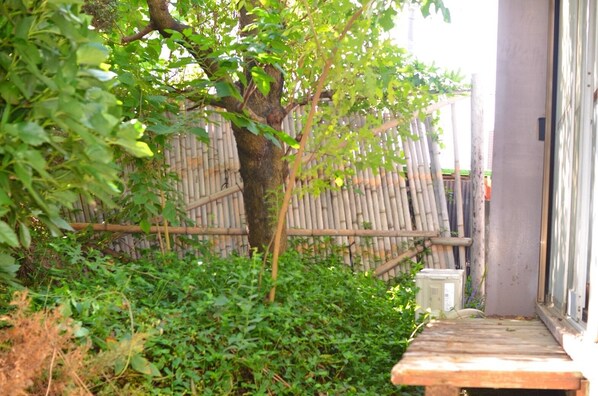 Un banco de madera en un jardín con follaje abundante y una valla de bambú al fondo.