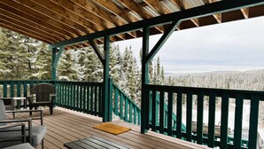 Une terrasse en bois avec des meubles d’extérieur, une vue sur des arbres couverts de neige et un ciel dégagé.