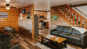 L’intérieur chaleureux d’un chalet, avec un décor en bois, un coin repas, un salon doté d’un canapé et une cuisine équipée de meubles en bois et d’un four à micro-ondes.