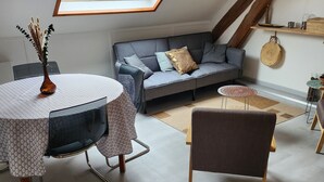 A cozy loft bedroom with a skylight, a gray sofa, a round table, and a chair. - 3-bedroom apartment, 2 steps from Chambord, Loire castles, Beauval (Tour-en-Sologne)