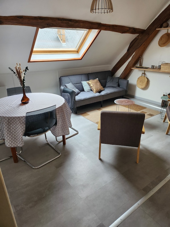 A cozy loft bedroom with a skylight, a gray sofa, a round table, and a chair.