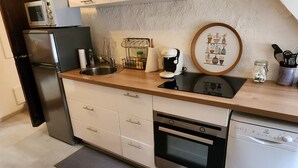A modern kitchen with a built-in oven, dishwasher, and microwave. There is a sink with a faucet, a countertop with a coffee maker, and a framed picture above the sink. - 3-bedroom apartment, 2 steps from Chambord, Loire castles, Beauval (Tour-en-Sologne)