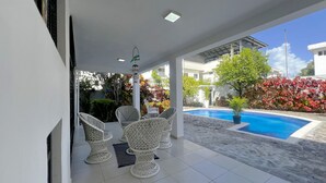 A covered outdoor area with a pool, white wicker furniture, and a view of a residential building. - 4-bedroom house in the middle of superb Sosúa with WiFi, AC (Sosúa)