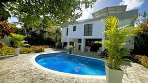 A swimming pool surrounded by a stone patio, with a white building in the background. - 4-bedroom house in the middle of superb Sosúa with WiFi, AC (Sosúa)
