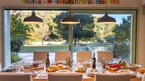 A dining table set for six with a view of a garden and a lake.