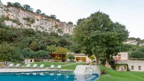 A pool area with lounge chairs, a stone building, and a large tree.