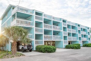 A multi-story hotel with balconies, a parked vehicle, and a palm tree.