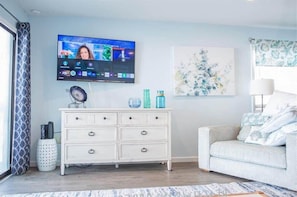 A living room with a flat-screen TV, a white dresser, a sofa, and a painting on the wall.