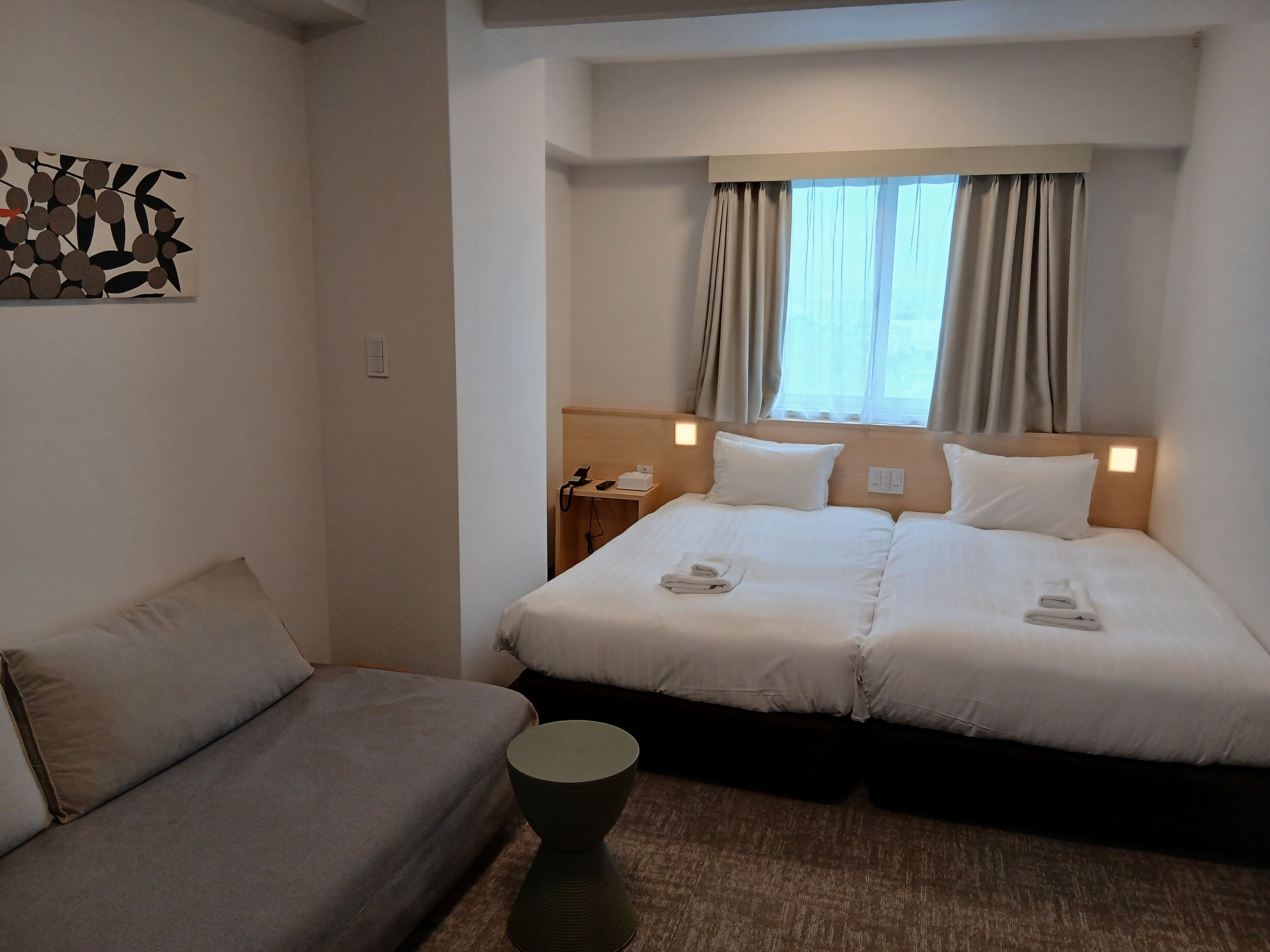 Een hotelkamer met een bed, een bank, een nachtkastje met telefoon en een raam met gordijnen.