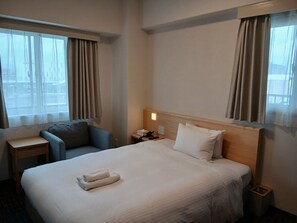 Una habitación de hotel con una cama, un escritorio, una silla y una mesita de noche.