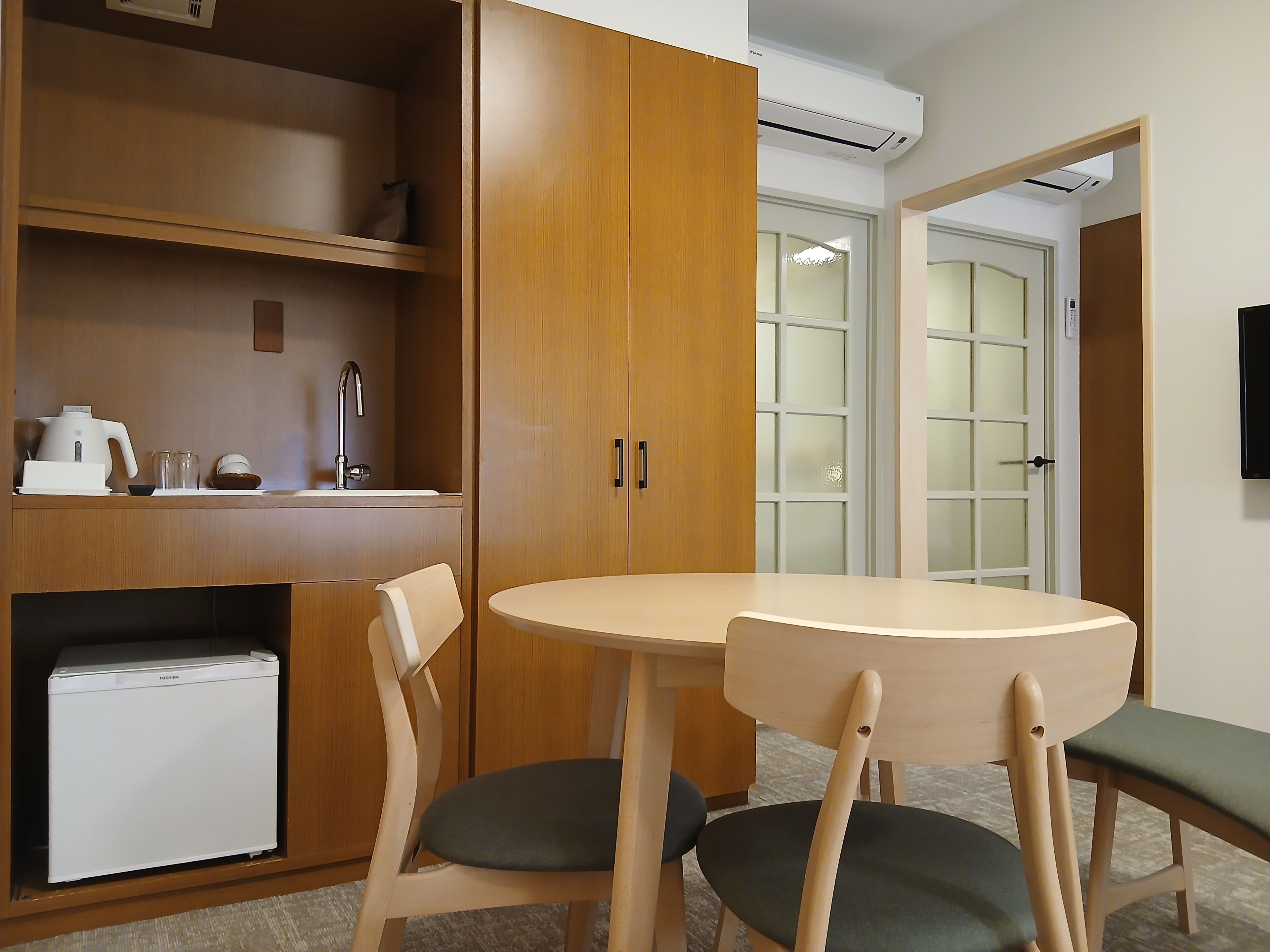 A compact room with a kitchenette, a dining table with chairs, and a built-in refrigerator.