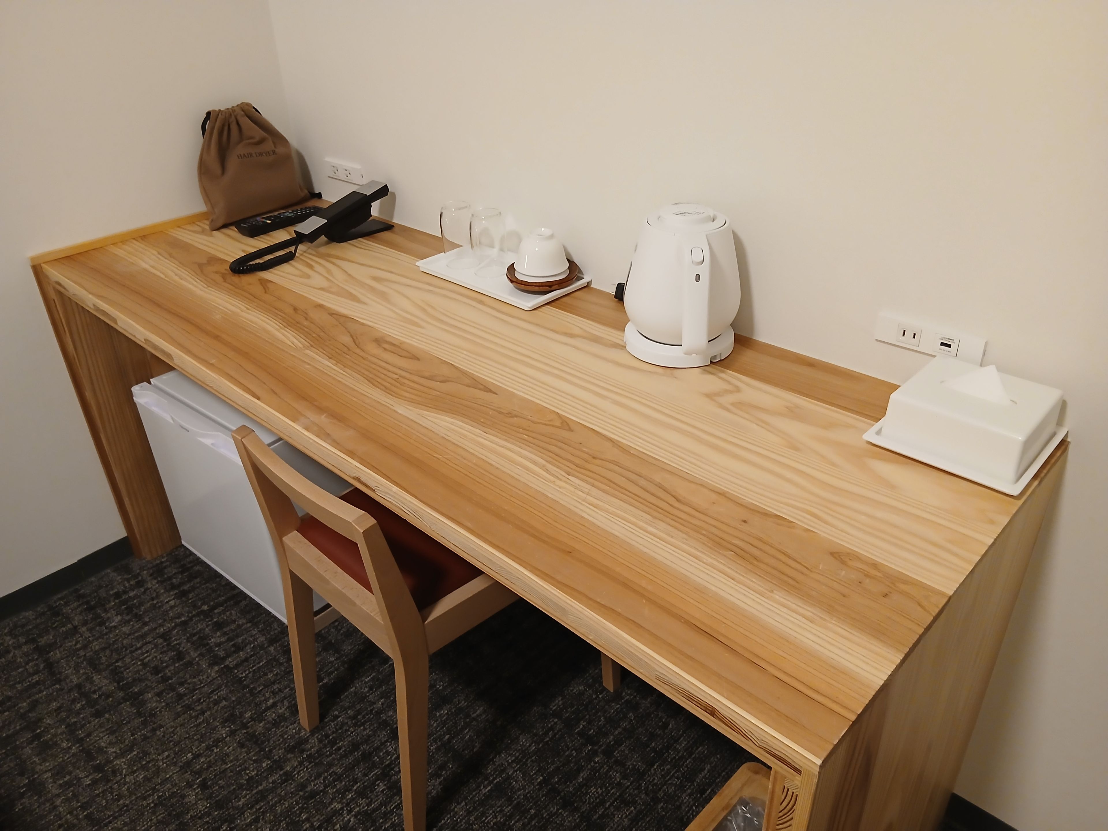 A wooden desk with a laptop, a remote control, a coffee maker, and a tissue box.