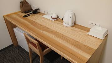 A wooden desk with a laptop, a remote control, a coffee maker, and a tissue box.
