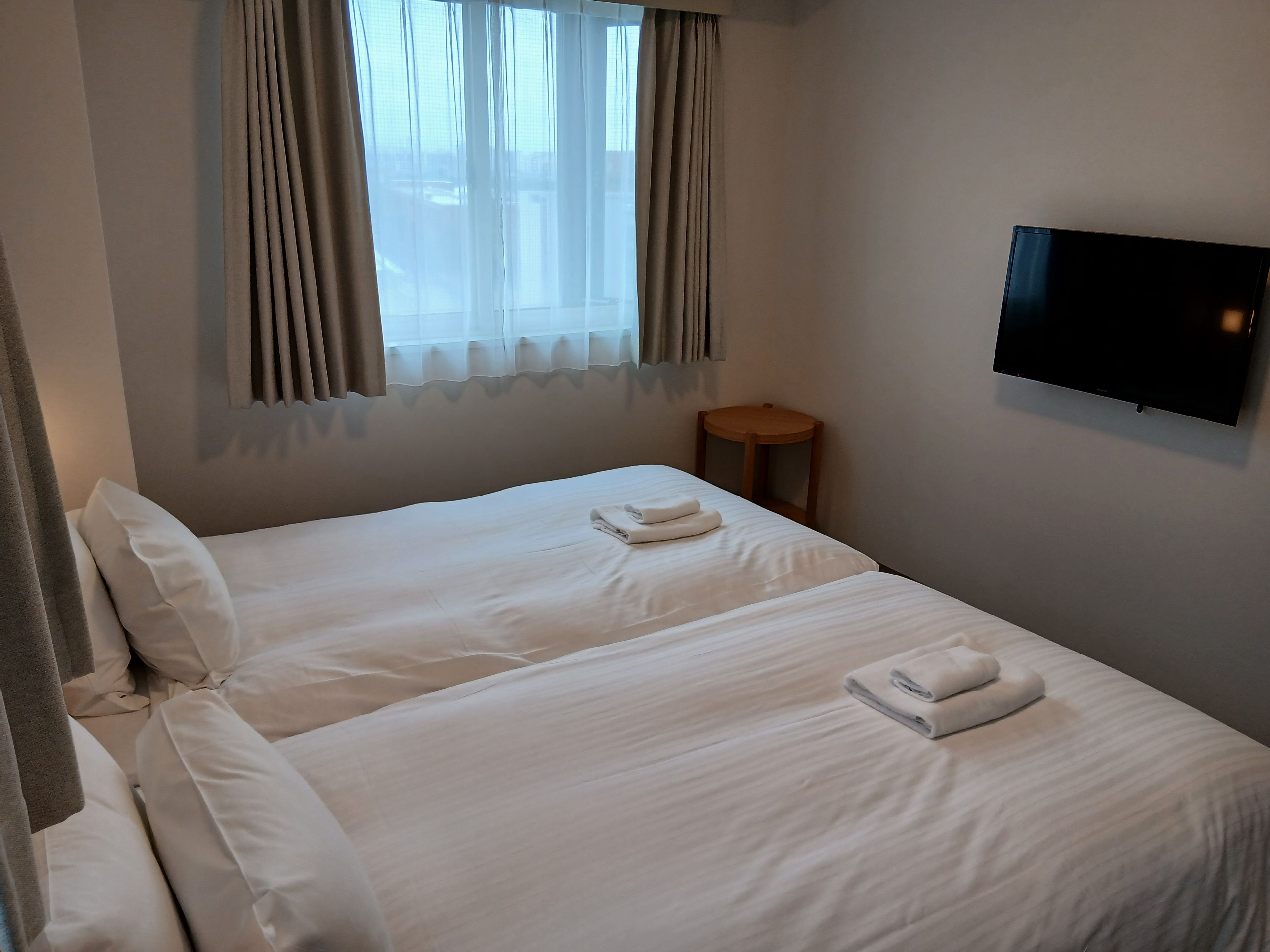 A hotel room with two beds, a TV on the wall, and a small wooden table.