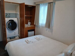 Ein Hotelzimmer mit einem Bett, einer Waschmaschine, einer kleinen Küchenzeile und einem Fenster mit Vorhängen.