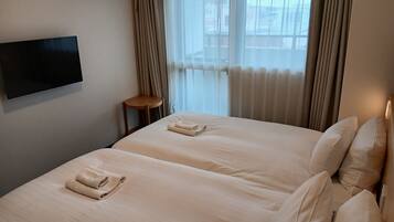 Habitació d'hotel amb llit, una cadira, televisió i finestra amb cortines.