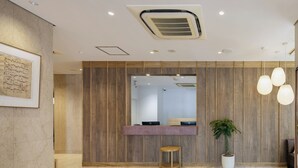 A modern reception area with a wooden panel wall, a reception desk, a potted plant, and a tiled floor.