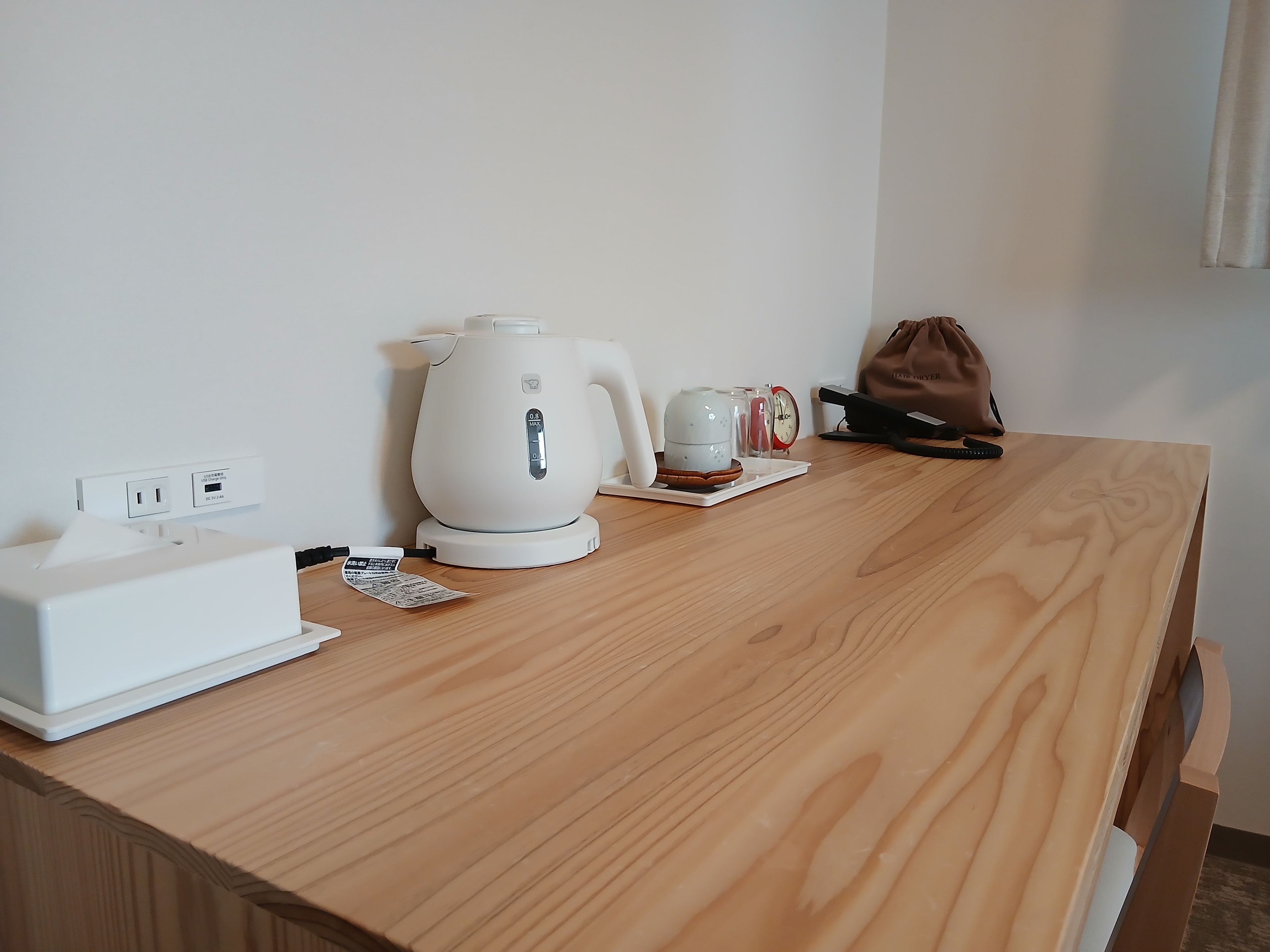 A wooden table with a white kettle, a small clock, and a bag.