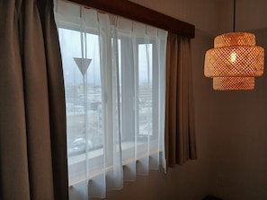 Una habitación con un ventanal grande, cortinas translúcidas y una lámpara colgante de fibra.