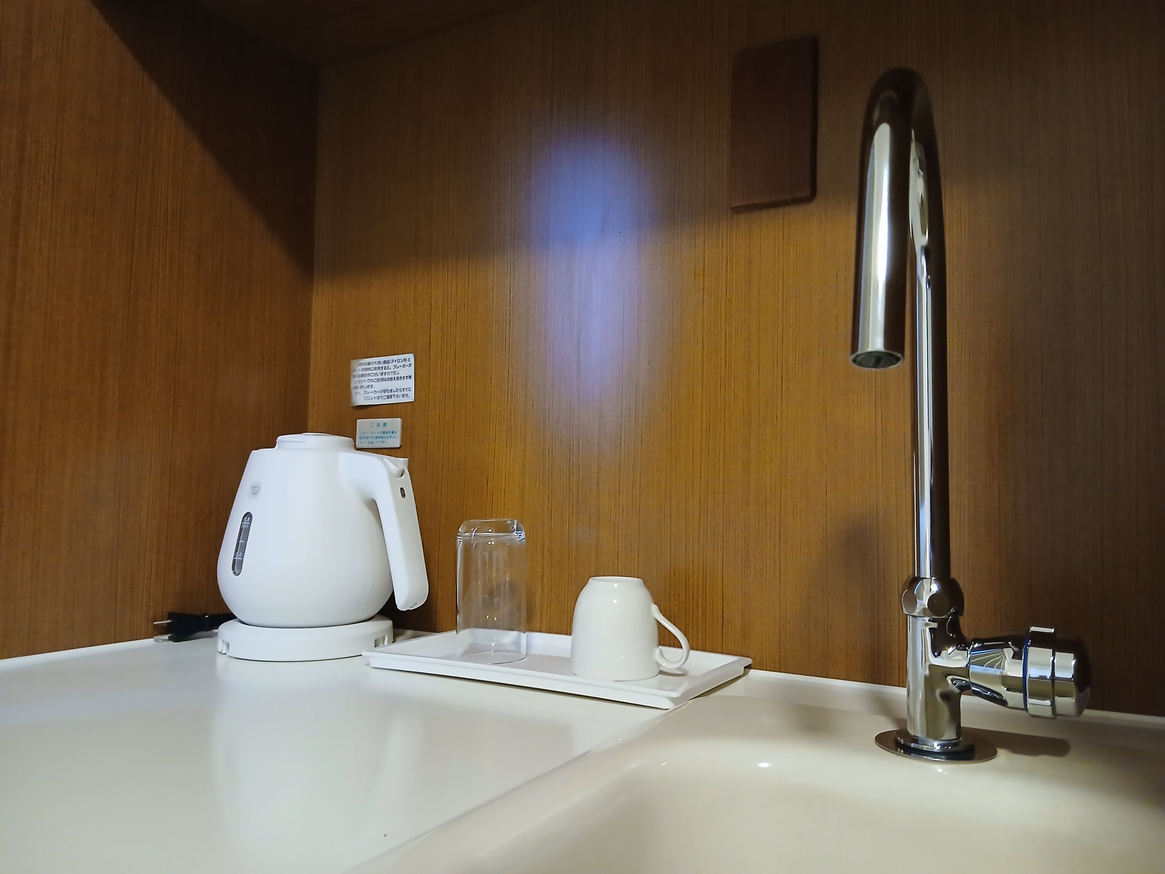 A hotel bathroom with a sink, a faucet, a coffee maker, and a glass.