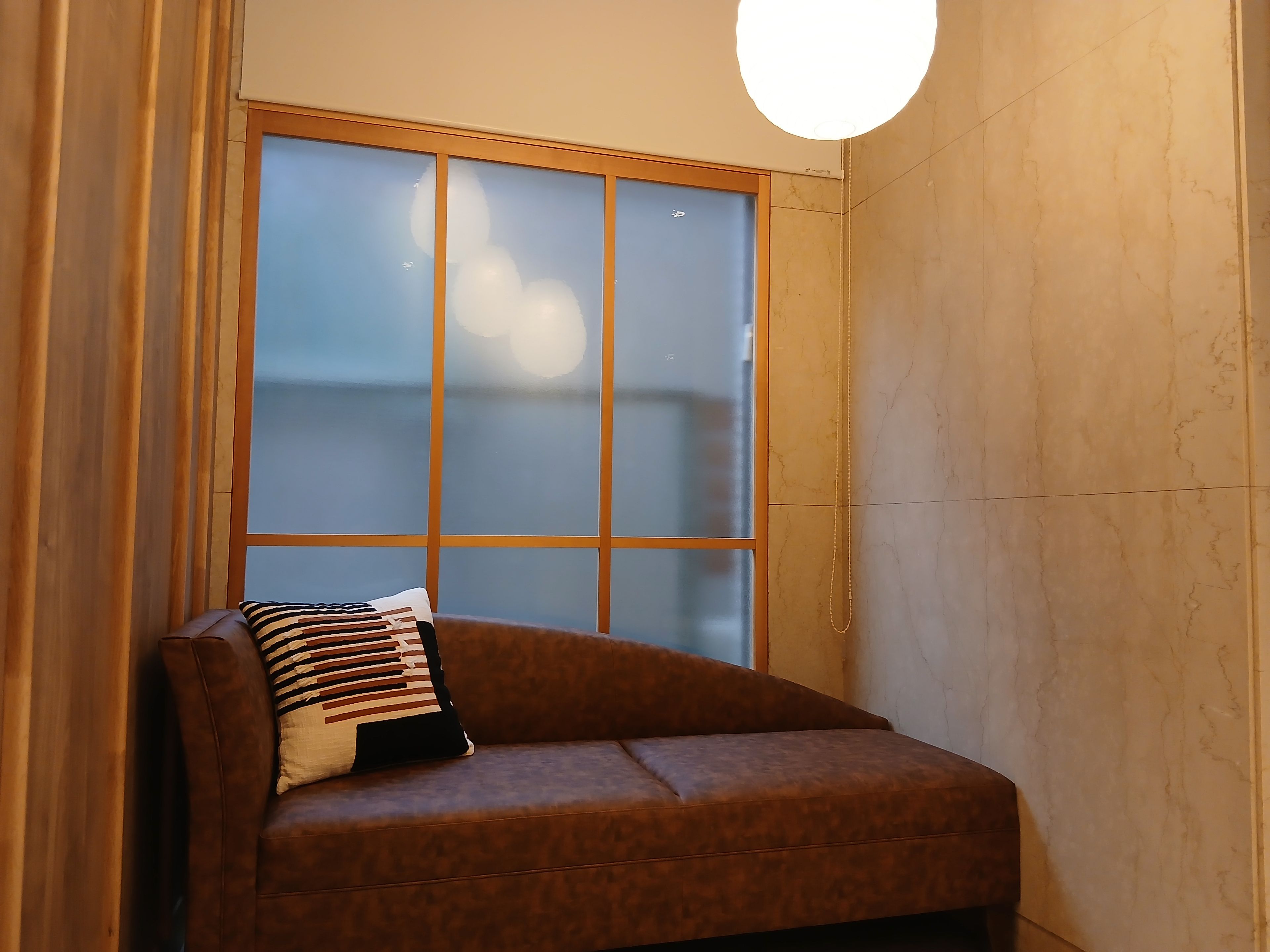 A corner room with a brown sofa, a patterned pillow, and a large window with a view.