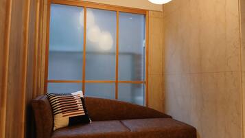 A corner room with a brown sofa, a patterned pillow, and a large window with a view.