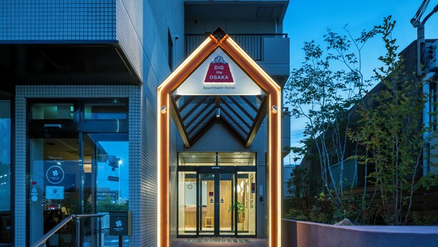 The entrance of the Dig the Osaka Apartment Hotel with a modern design, including a glass door and a sign above the entrance.