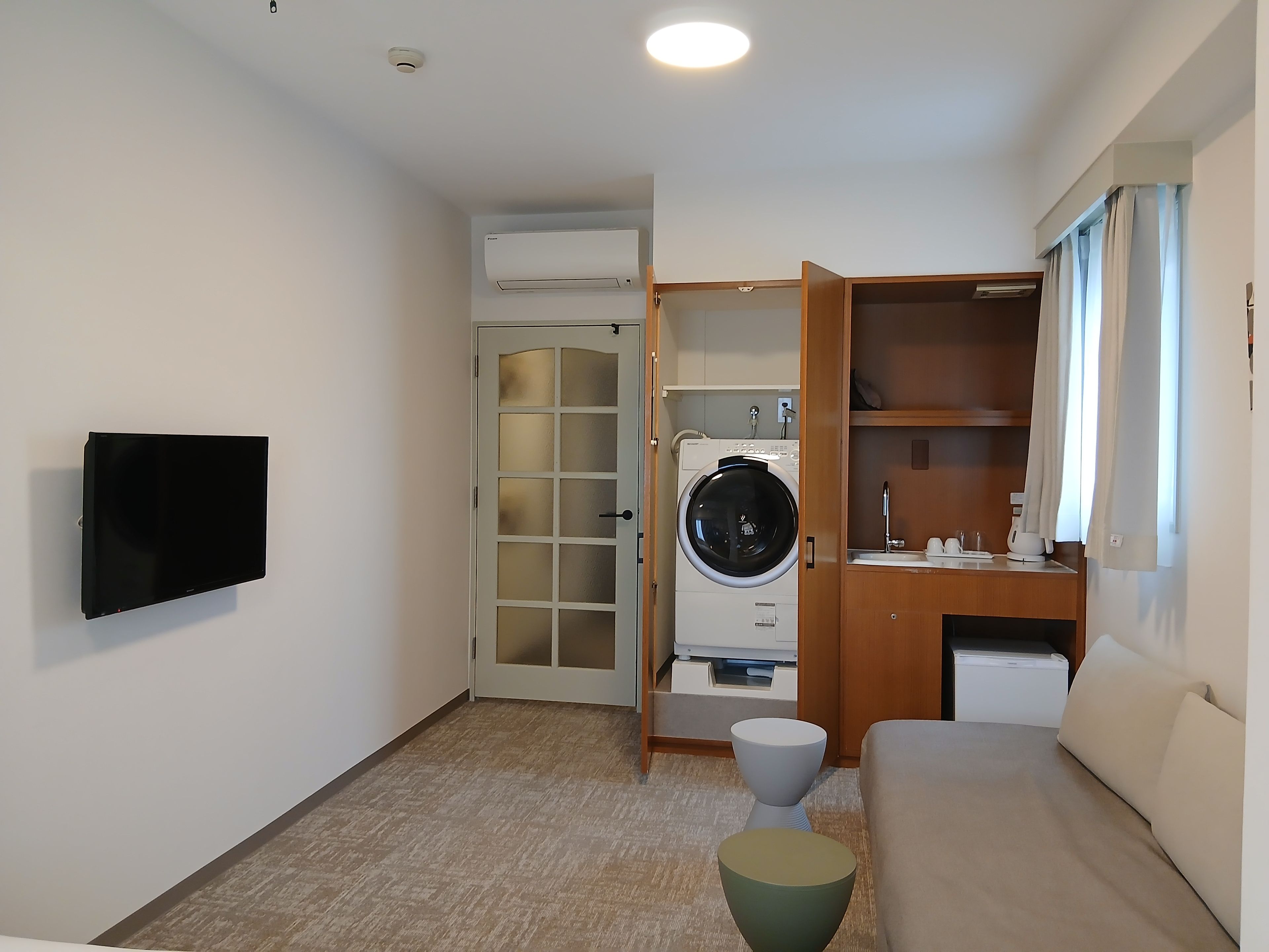 Un ambiente compatto con TV a schermo piatto fissata al muro, lavatrice, un tavolino e un divano.
