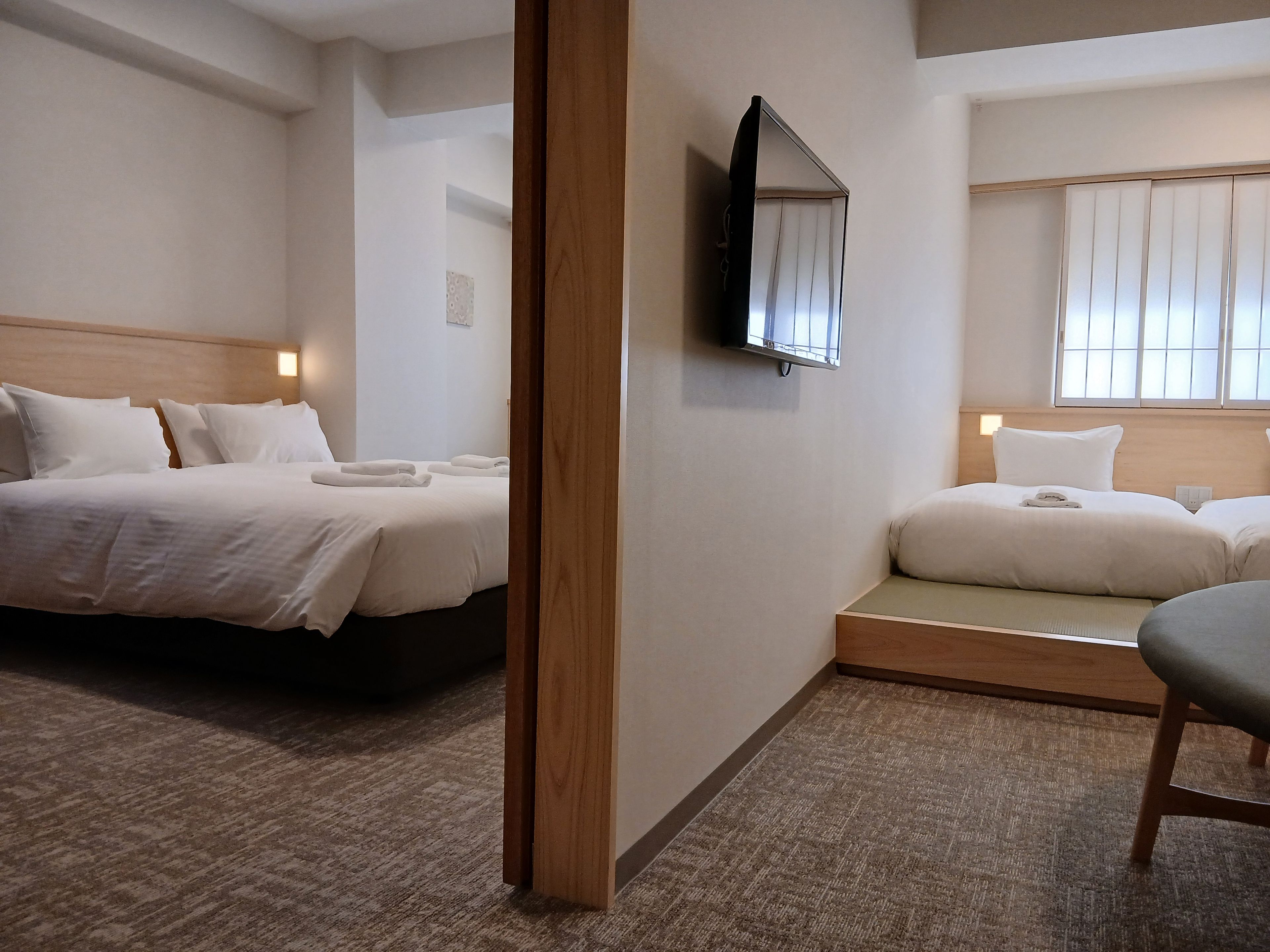 Une chambre d’hôtel avec deux lits, un téléviseur fixé au mur et une fenêtre avec des rideaux.