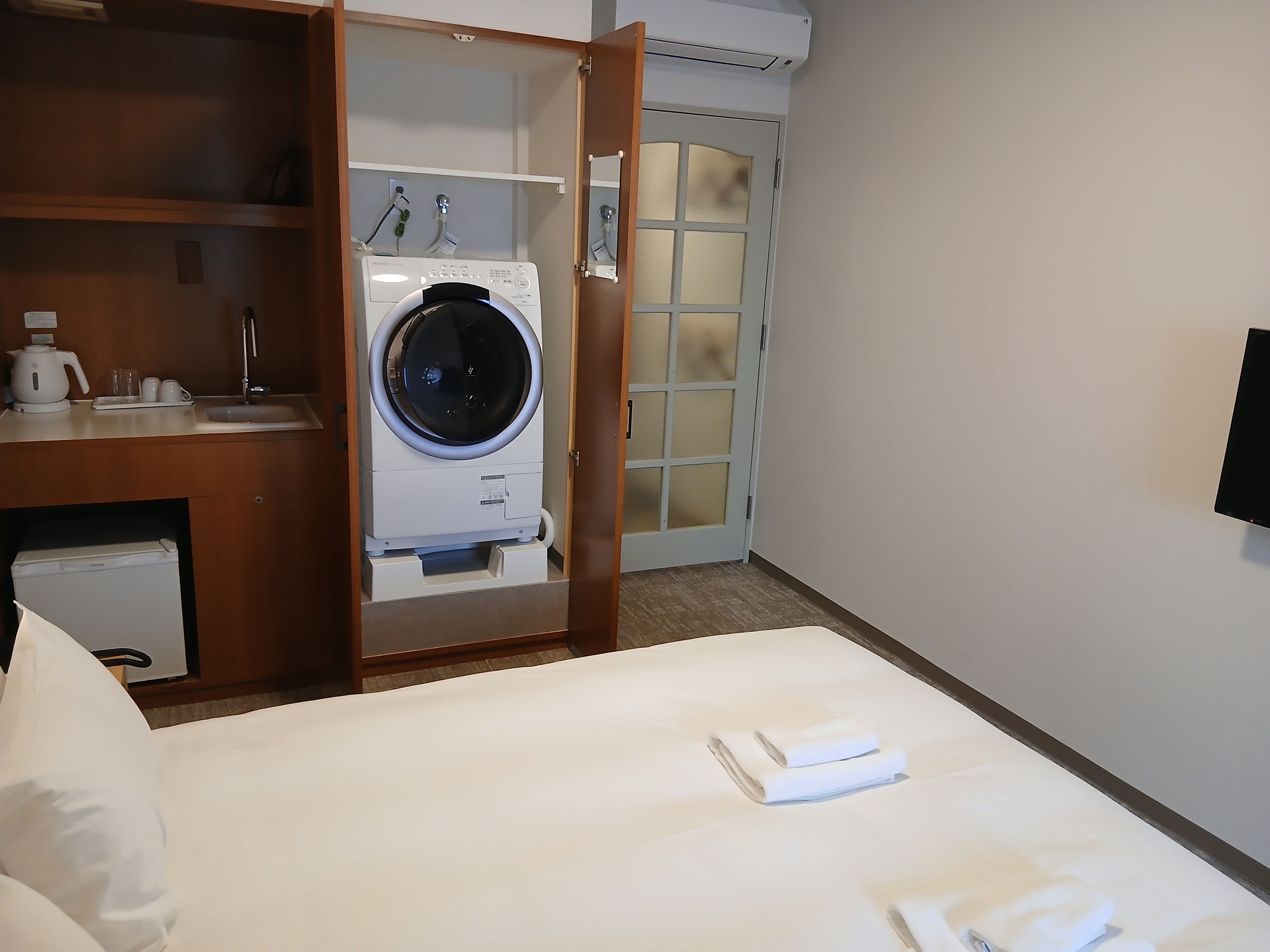 A hotel room with a bed, a washing machine, a sink, and a mirror.