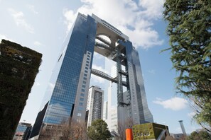 A modern high-rise building with a distinctive arch structure, surrounded by trees and other buildings. - Apartment Hotel DIG the OSAKA (Suita)