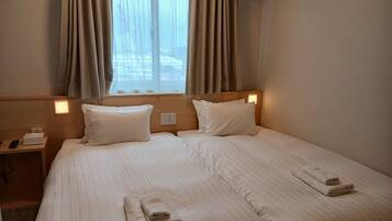 Ein Hotelzimmer mit einem großen Bett, zwei Kissen, einem Nachttisch mit Telefon und Lampe sowie einem Vorhangfenster.