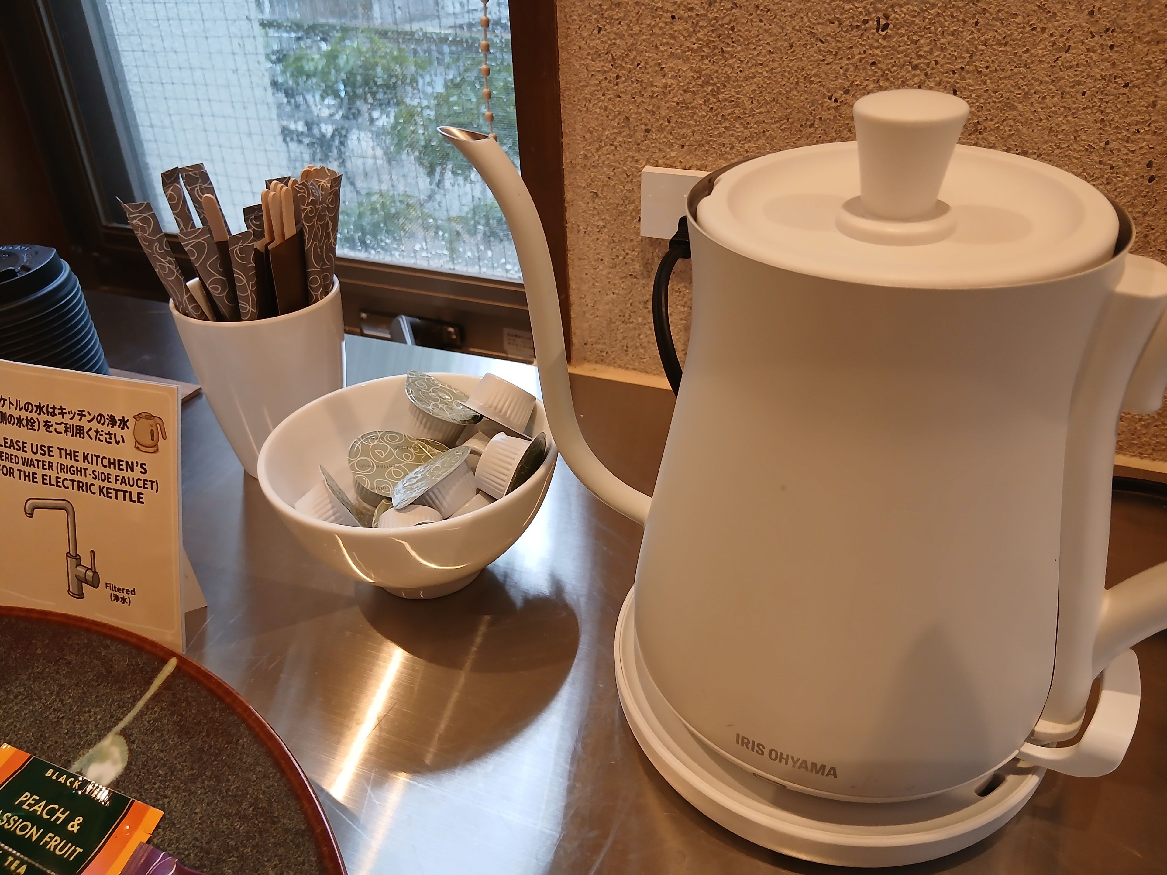 A kitchen area with a white electric kettle, a bowl with tea bags, and a sign indicating the use of filtered water for the kettle.