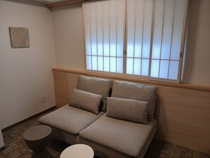 Una habitación con un sofá, una mesita redonda y una ventana con persianas.