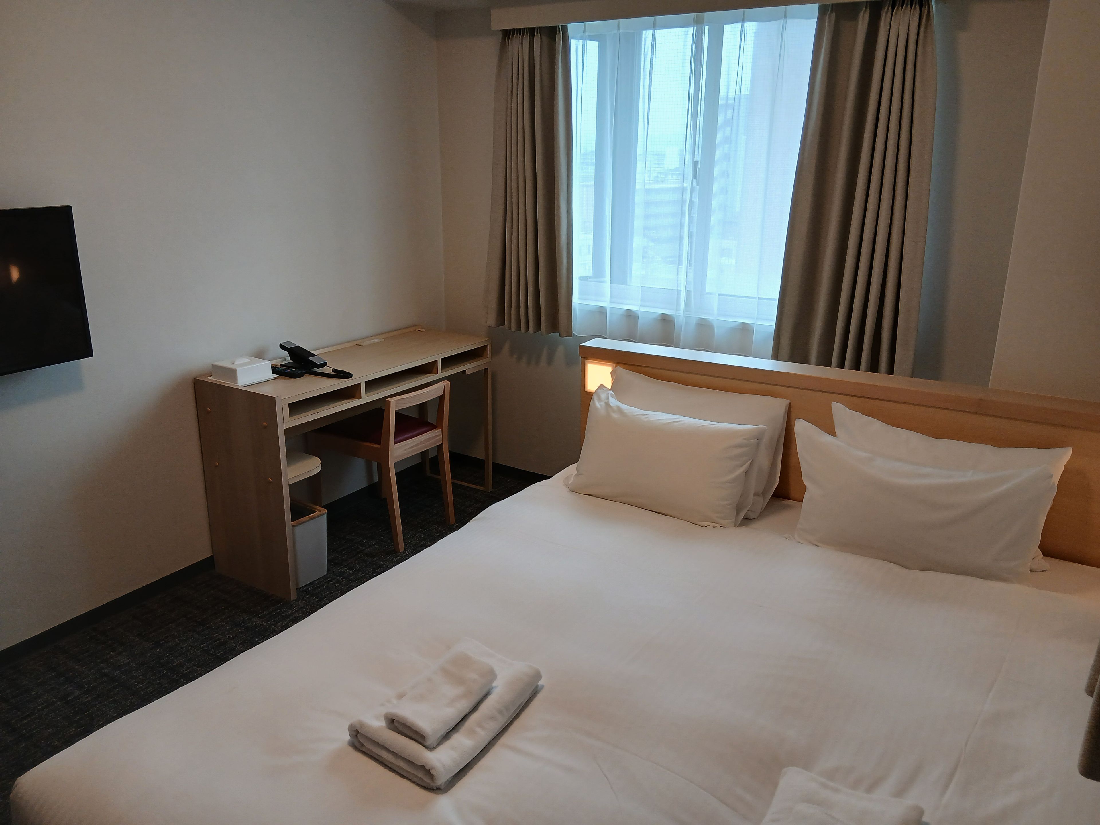 A hotel room with a bed, a desk, a chair, and a TV.