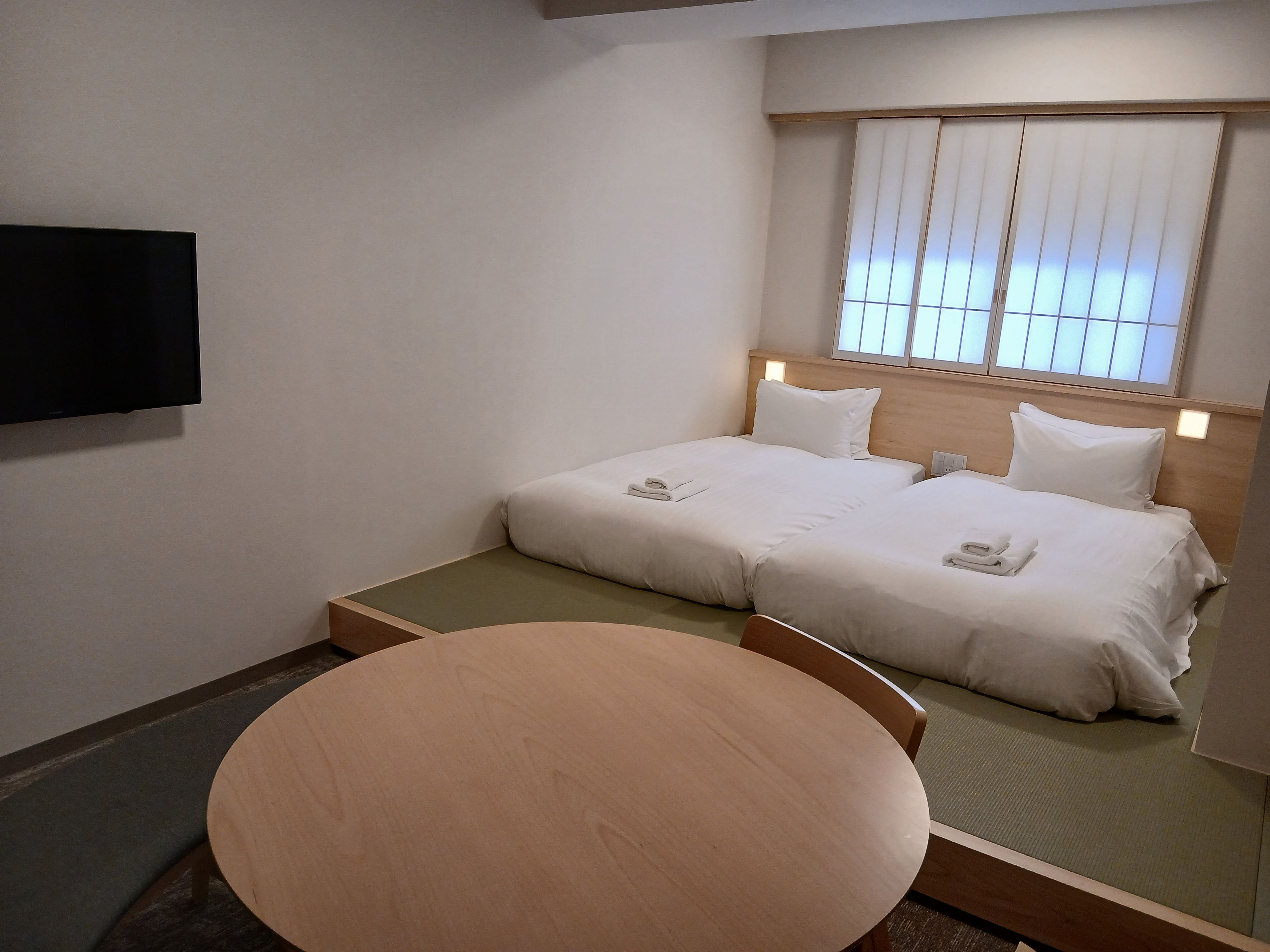 Quarto de hotel com uma cama, televisão e uma mesa redonda.
