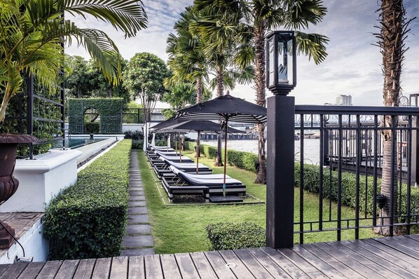 Un espace aménagé au bord de la piscine, avec des chaises longues, des parasols et une vue sur l’eau.