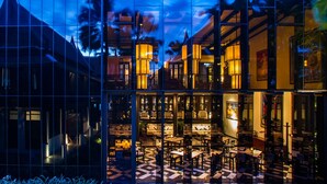 Un edificio moderno con fachada de vidrio que refleja el interior. En su interior, hay varias zonas de comedor con mesas y sillas.