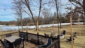 A deck with outdoor seating, a view of a river, and trees. - Remodeled Home on Wooded Nagawicka Lake Channel (Delafield)