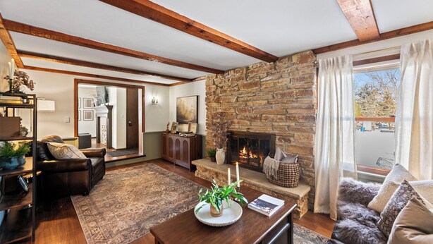 A cozy living room with a stone fireplace, leather furniture, and a large window with curtains. - Remodeled Home on Wooded Nagawicka Lake Channel (Delafield)