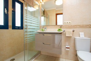 A bathroom with a glass shower enclosure, a sink with a decorative mirror above it, and a toilet.