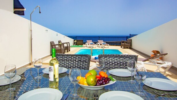 A dining table set with plates, wine glasses, and a fruit bowl, overlooking a pool with lounge chairs. - Casa Yaiza - Three Bedroom Villa, Sleeps 6 (Puerto Calero)