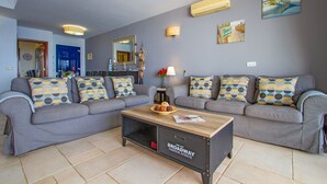 A modern living room with grey sofas, patterned cushions, a wooden coffee table, and a wall-mounted air conditioner. - Casa Yaiza - Three Bedroom Villa, Sleeps 6 (Puerto Calero)
