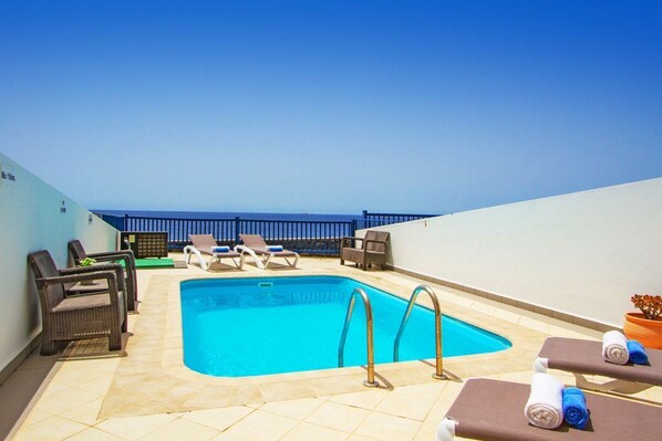 A rooftop pool area with lounge chairs, a pool, and a view of the sea.
